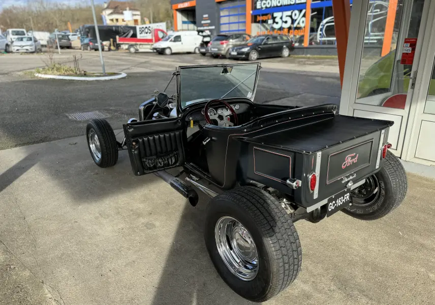 Ford T Hot Rod V8 noir vue 3/4 arrière droit, capote manuelle ouverte et intérieur cuir visible.