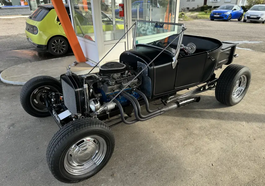 Ford T Hot Rod V8 noir, vue 3/4 avant droit, capote décapotée et moteur V8 apparent avec échappements latéraux.