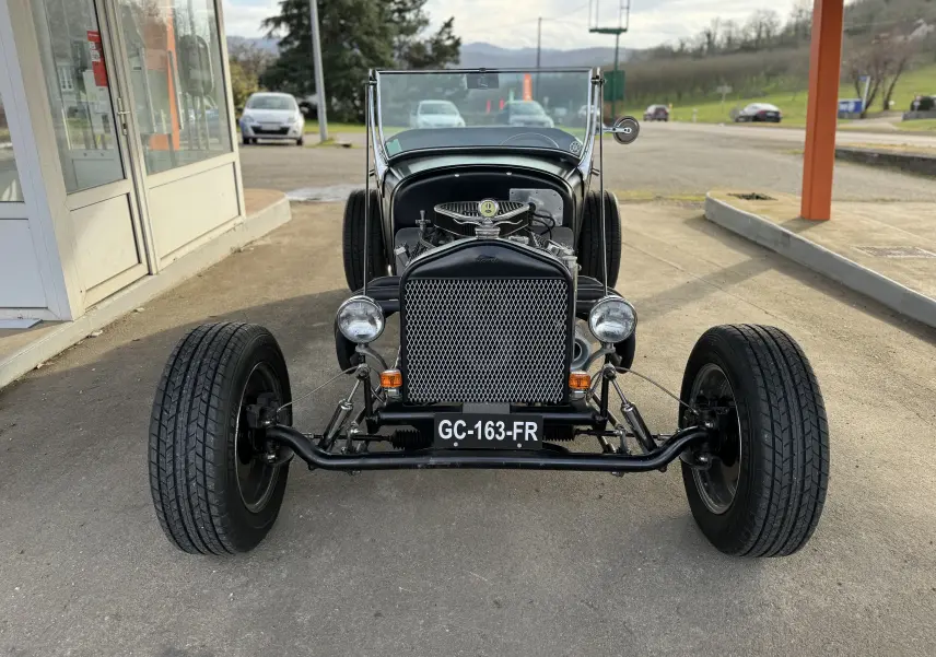Vue frontale d'une Ford T Hot Rod V8 noire de 1923, avec calandre ajourée et moteur apparent sous un pare-brise bas.