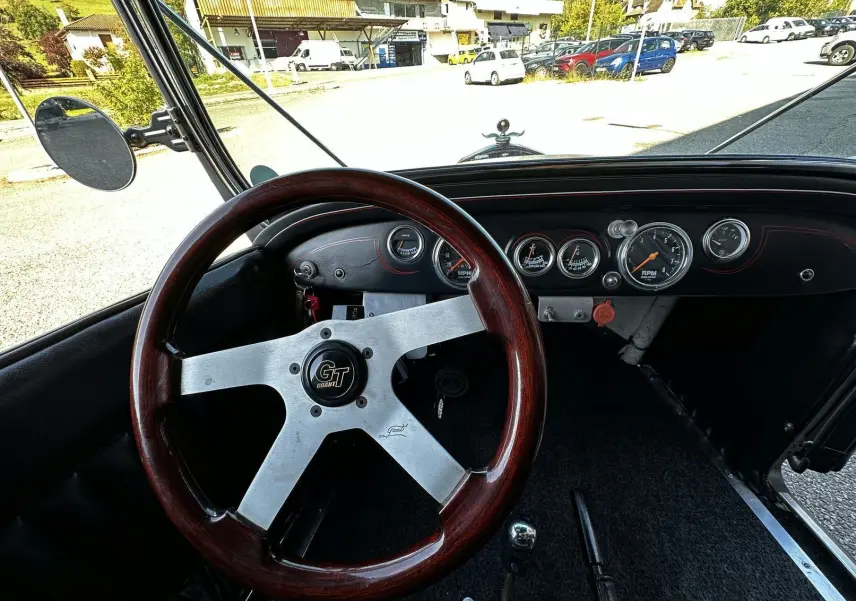 Vue intérieure du volant bois GT et tableau de bord noir du Ford T Hot Rod V8 de 1923 avec compteurs ronds visibles.