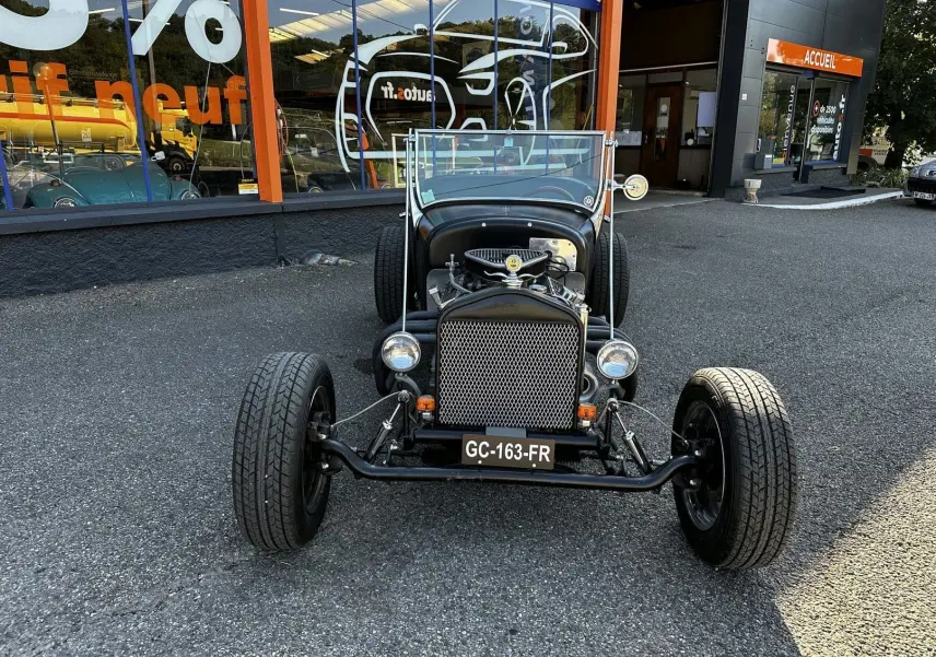 Ford T Hot Rod V8 noir vue de face, capot ouvert dévoilant le moteur et calandre en métal ajouré.