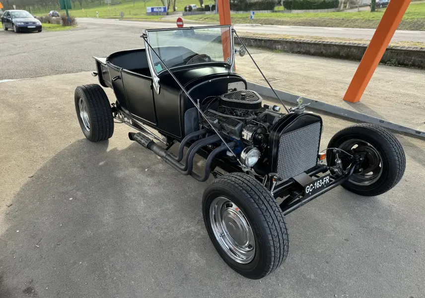 Ford T Hot Rod V8 noir vue 3/4 avant droit, moteur V8 apparent et carrosserie décapotable classique.