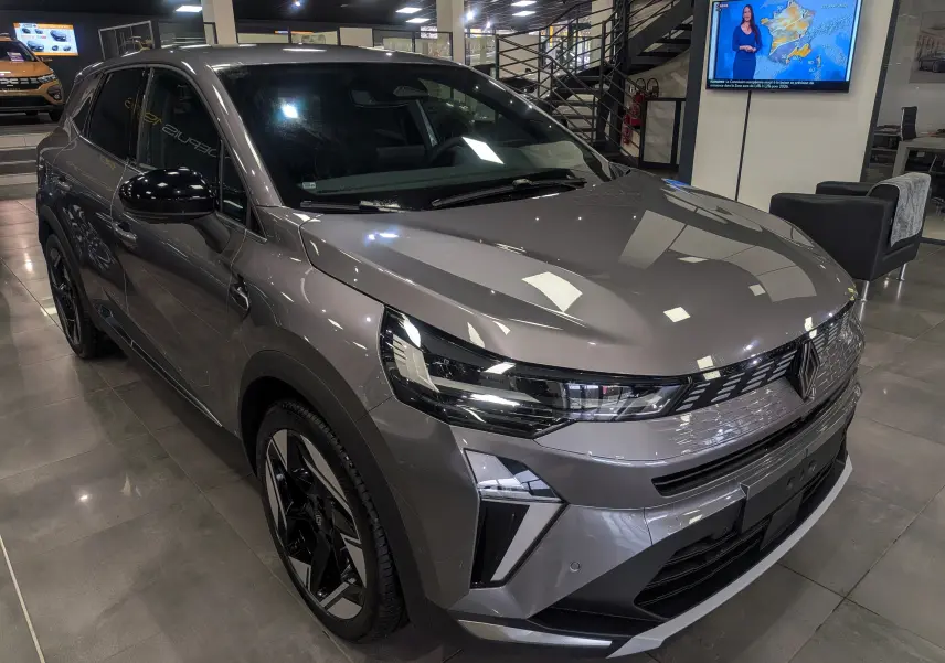 Renault Symbioz E-Tech gris Cassiopé en 3/4 avant droit, avec phares LED et jantes bicolores en showroom.