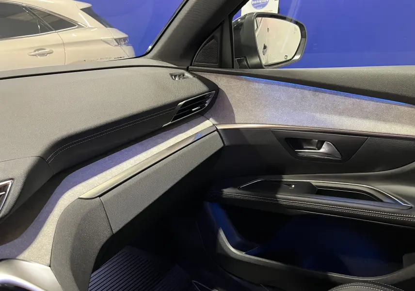 Intérieur du Peugeot 5008 GT 2024, vue rapprochée du volant et console centrale avec éclairage bleu subtil.