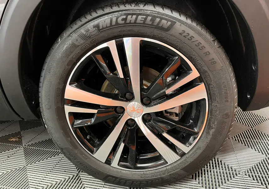Gros plan sur la jante alliage bicolore noire et argent avec logo Peugeot, montée sur un pneu Michelin 225/55 R18.