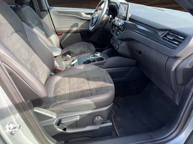 Vue intérieure côté conducteur du Ford Kuga 2024 gris, avec sièges en tissu et cuir, console centrale et écran tactile visible.