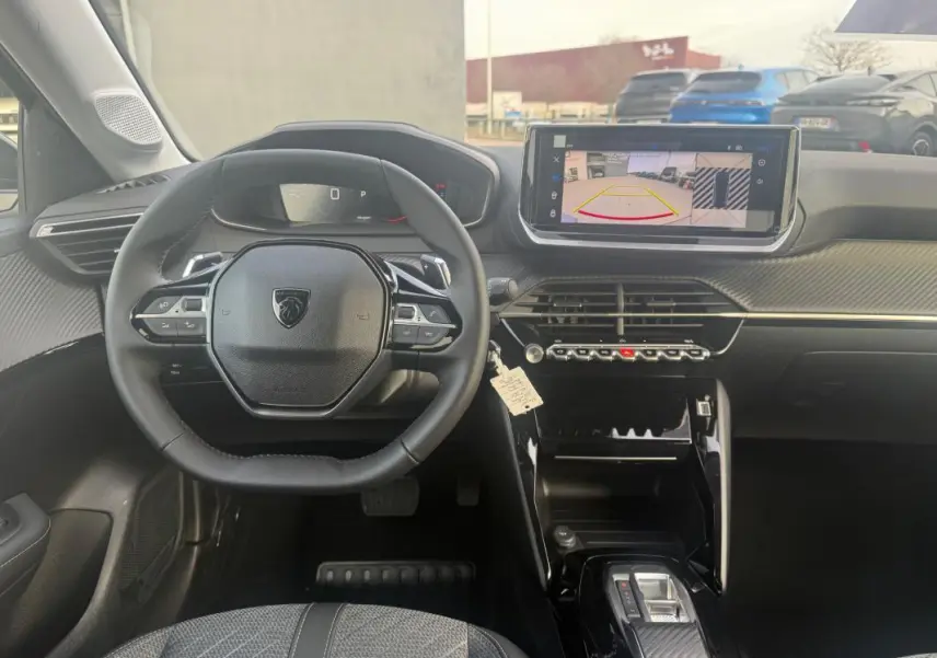 Vue intérieure du poste de conduite de la Peugeot 208 Hybrid 110 e-DCS6 Allure 2025, avec volant compact et écran tactile affichant la caméra de recul.