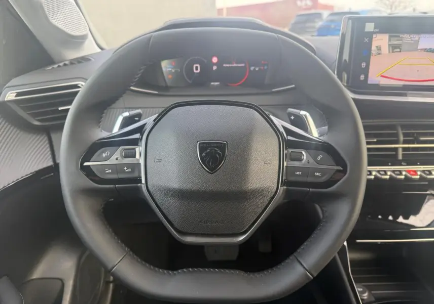 Vue intérieure centrée sur le volant noir de la Peugeot 208 Hybrid 110, avec tableau de bord numérique et écran tactile visible.