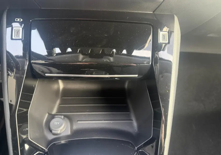 Vue rapprochée de la console centrale noire brillante du Peugeot 208 gris, avec prise 12V visible en bas.