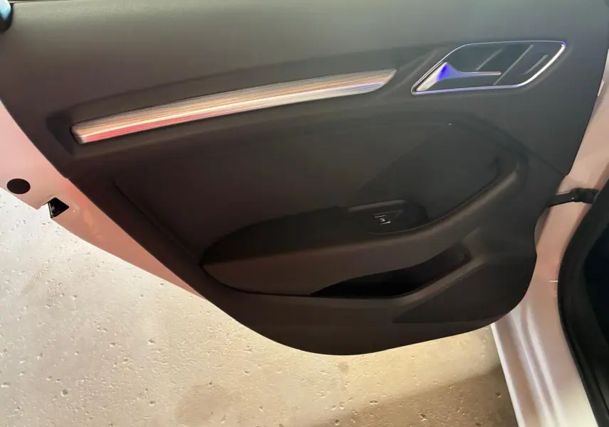 Vue intérieure de la porte côté gauche d'une Audi A3 Sportback blanche, avec garniture noire et insert décoratif argenté.