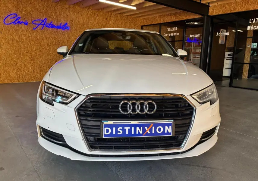 Vue de face d'une Audi A3 Sportback blanche 2019 avec calandre noire et logo Audi visible en intérieur showroom.