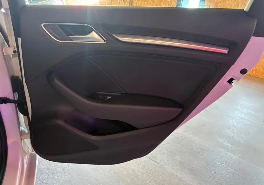 Vue intérieure de la porte arrière gauche noire d'une Audi A3 Sportback blanche, avec poignée et commande de fenêtre.