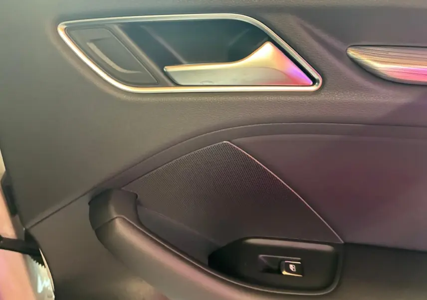 Détail de la poignée intérieure côté gauche en plastique noir avec insert chromé sur une Audi A3 Sportback blanche.