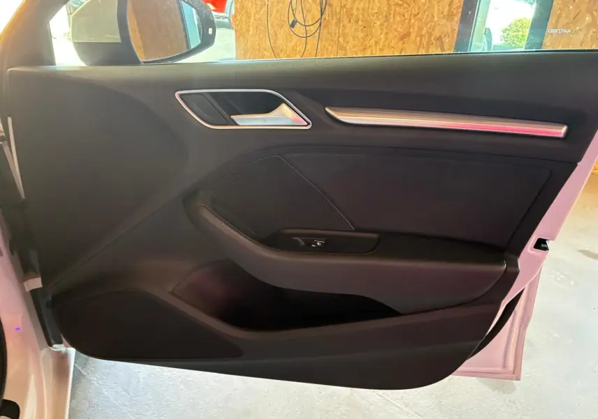 Vue intérieure de la porte avant gauche noire de l'Audi A3 Sportback blanche, avec poignée et commande de fenêtre.