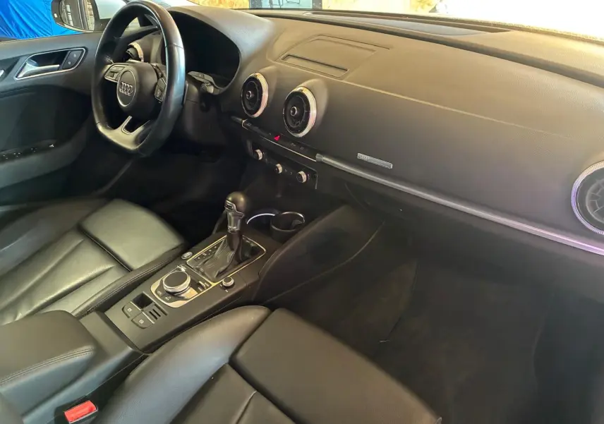 Vue intérieure côté conducteur de l'Audi A3 Sportback 2019, tableau de bord noir avec volant et console centrale en cuir.