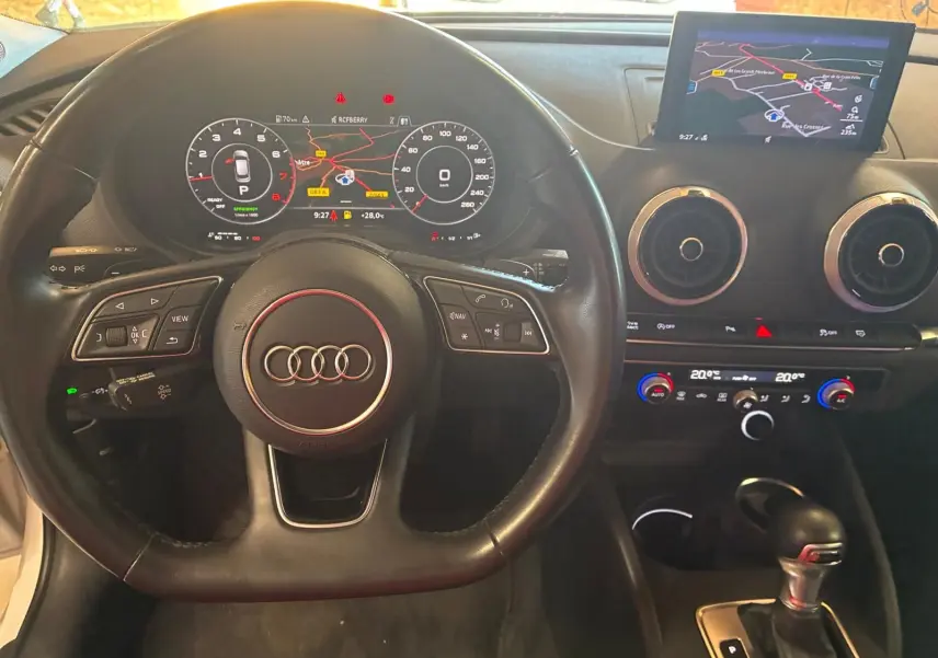 Vue intérieure centrée sur le volant et le tableau de bord noir de l'Audi A3 Sportback avec écran GPS et commandes intégrées.