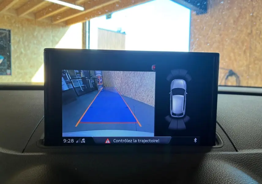 Écran central de l’Audi A3 Sportback blanc montrant la caméra de recul avec guidage de trajectoire et vue 360° du véhicule.