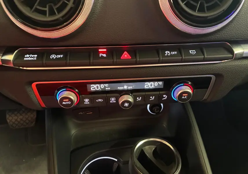 Vue rapprochée du tableau de bord de l’Audi A3 Sportback blanc, avec commandes climatisation et boutons de sécurité éclairés.