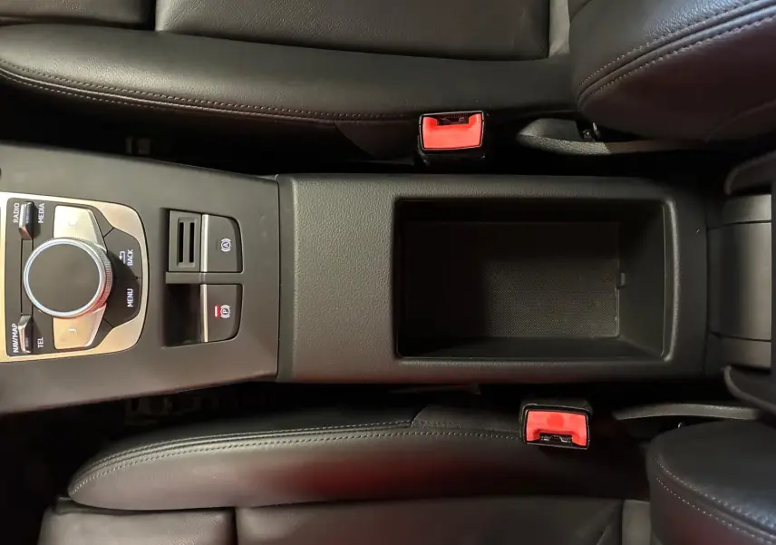 Vue plongeante sur la console centrale noire en cuir de l'Audi A3 Sportback, avec commandes multimédia et ceintures rouges.