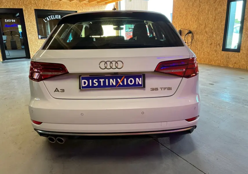 Vue arrière d'une Audi A3 Sportback blanche 35 TFSI avec double sortie d'échappement, stationnée en intérieur.