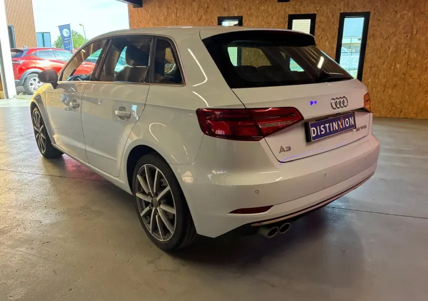 Audi A3 Sportback blanc vue 3/4 arrière droit en intérieur, avec jantes alliage et double sortie d’échappement.
