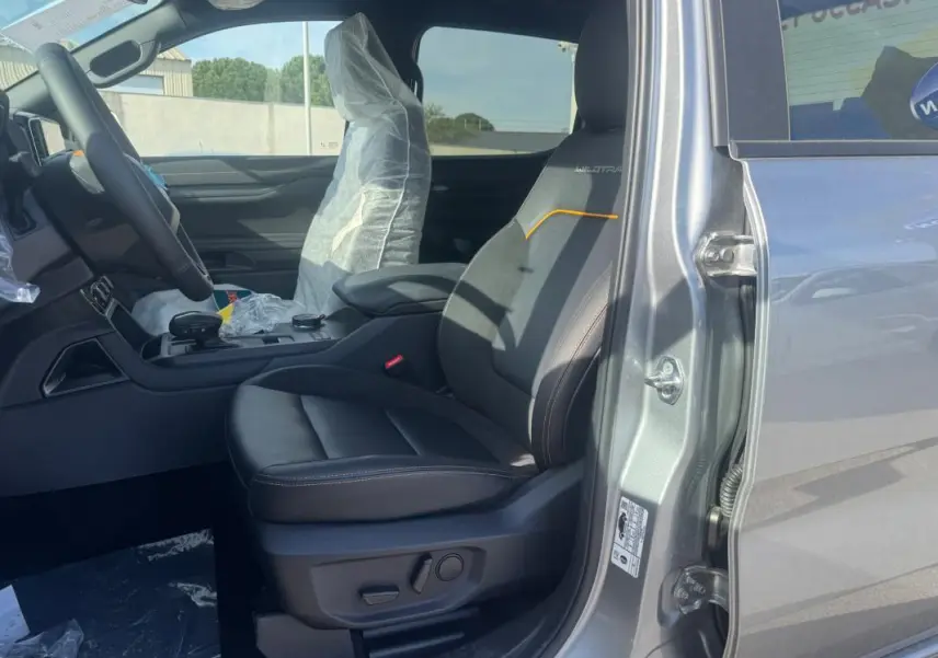Vue intérieure côté conducteur du Ford Ranger gris 2025, siège Wildtrak avec surpiqûres orange et accoudoir central.