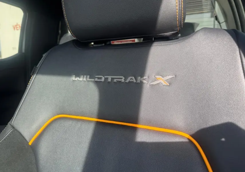 Gros plan sur le siège avant noir avec surpiqûres orange et logo Wildtrak X brodé du Ford Ranger gris.