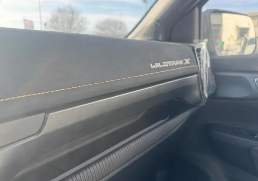 Vue intérieure côté passager du tableau de bord noir avec logo Wildtrak X et surpiqûres orange du Ford Ranger gris 2025.