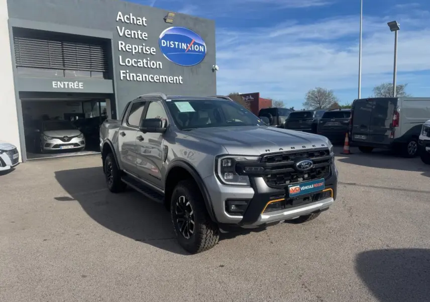 Ford Ranger Wildtrak gris en 3/4 avant droit, avec jantes alliage noires et barres de toit visibles.