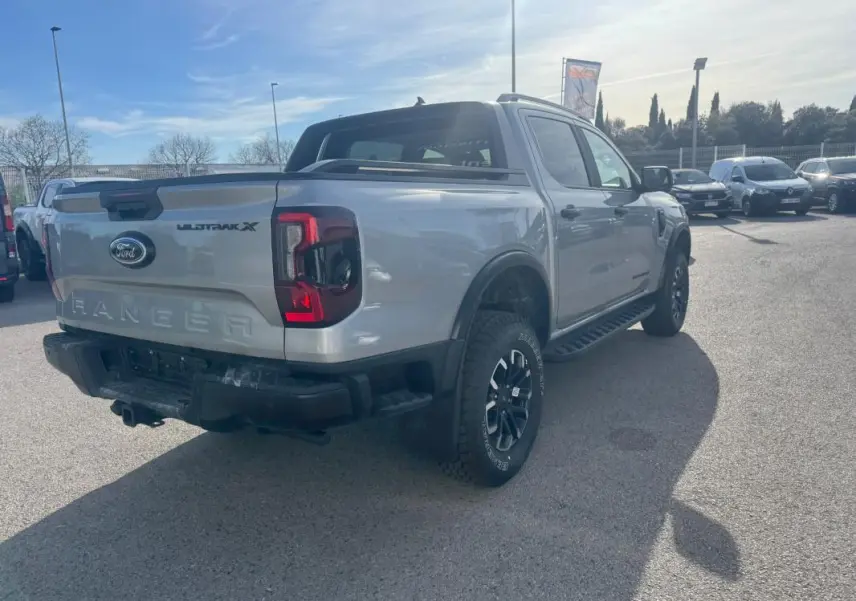 Vue 3/4 arrière droite d'un Ford Ranger gris 2025 Wildtrak X avec jantes alliage noires et barres de toit.