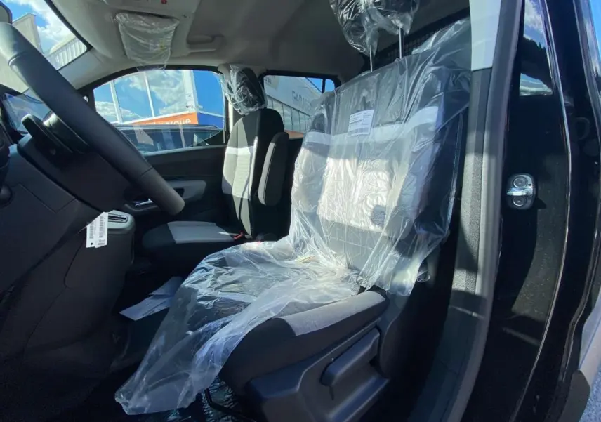 Vue intérieure côté conducteur du Citroën Berlingo noir 2026, sièges avant protégés par film plastique.