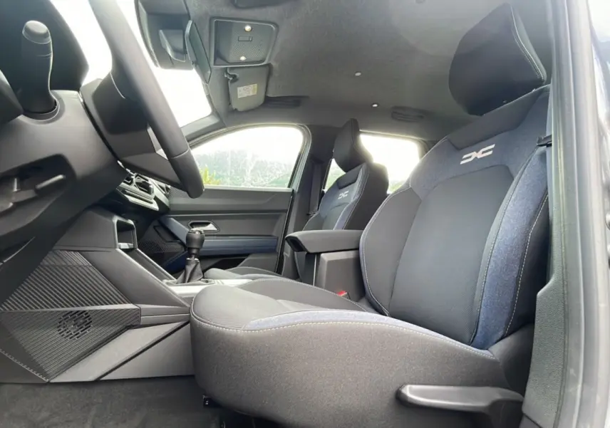 Intérieur avant du Dacia Bigster gris schiste, sièges tissu avec logo DC et levier de vitesses manuel visible.