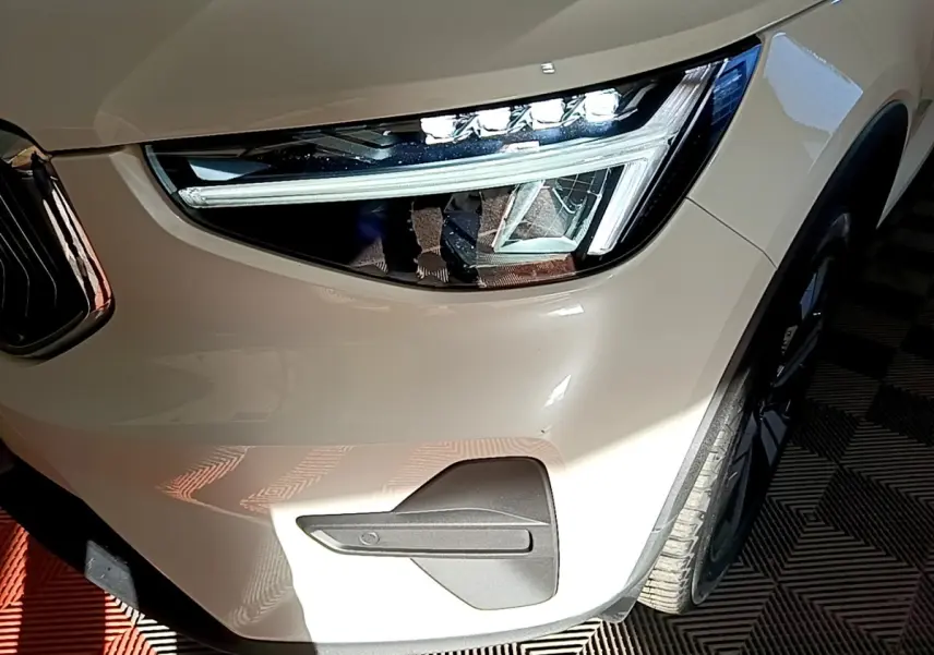 Gros plan sur le phare avant droit d’un Volvo XC40 Recharge T5 262 DCT7 Plus beige avec détails LED et partie de la roue.