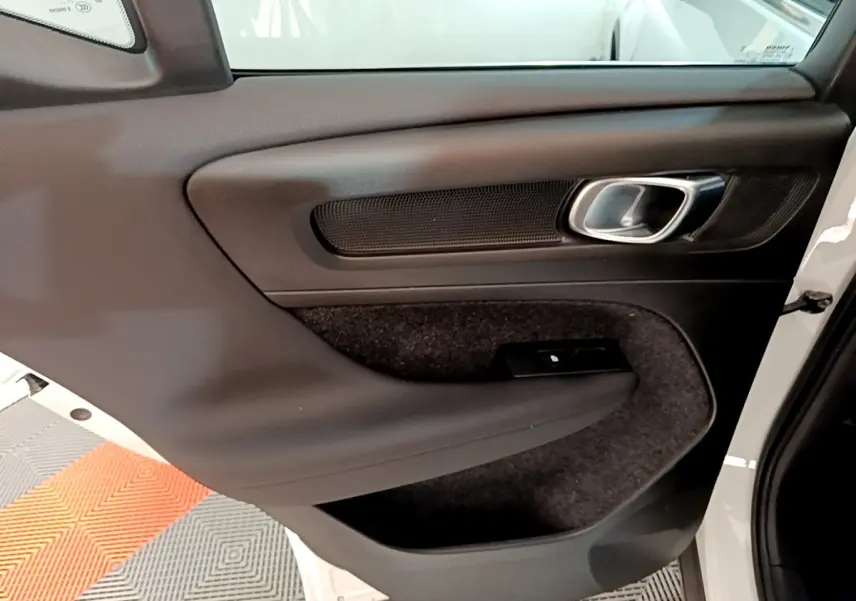 Vue intérieure côté gauche de la porte avant d’un Volvo XC40 Recharge T5 262 DCT7 Plus avec garniture noire et poignée métallique.