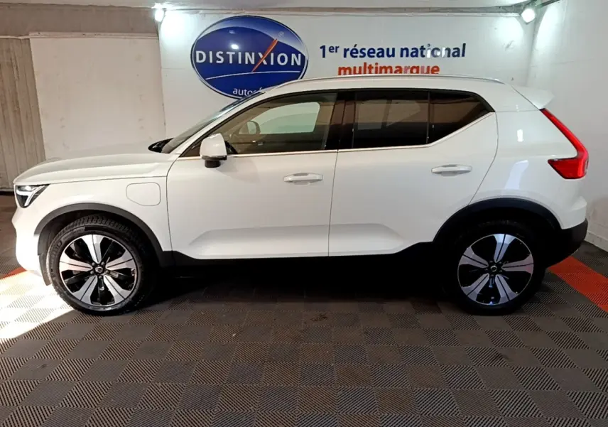 Vue latérale droite d'un Volvo XC40 hybride rechargeable blanc avec jantes noires et grises, dans un showroom.