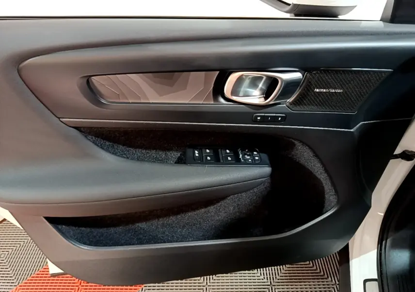 Vue intérieure côté gauche de la porte avant d’un Volvo XC40 blanc avec panneau noir et haut-parleur Harman/Kardon.