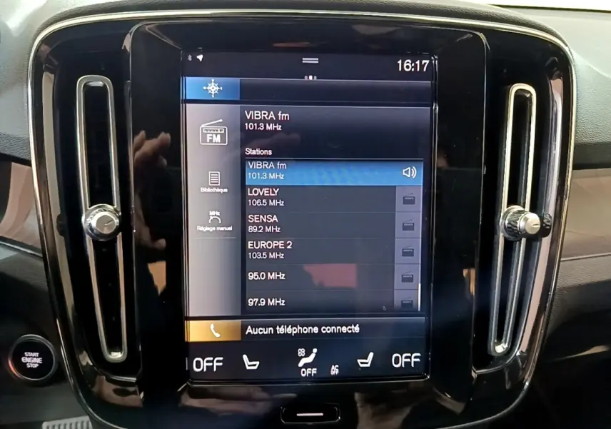 Vue frontale du tableau de bord noir du Volvo XC40 Recharge T5 avec écran tactile central affichant les stations radio.