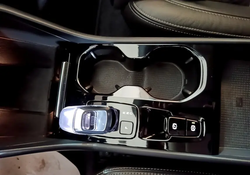 Vue plongeante sur la console centrale noire brillante du Volvo XC40 Recharge T5 avec levier de vitesses cristal et porte-gobelets.