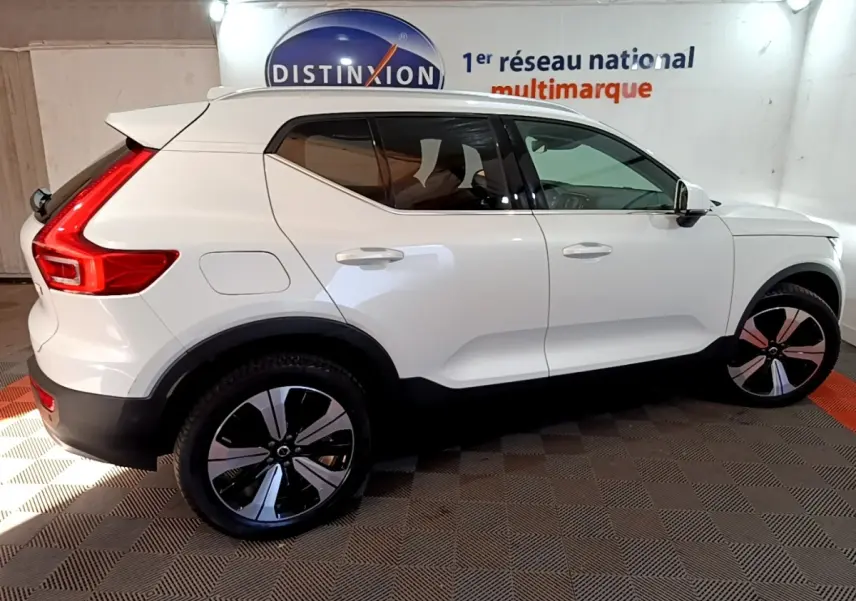 Vue de profil côté droit d'un Volvo XC40 Recharge T5 blanc avec jantes noires et rouges, stationné en intérieur.