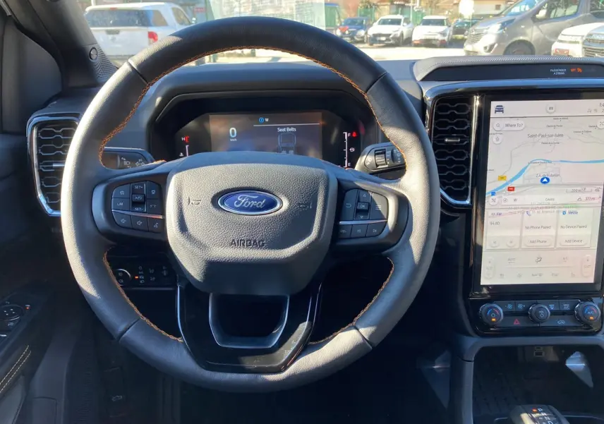 Vue intérieure centrée sur le volant cuir noir avec coutures marron et écran tactile vertical du Ford Ranger gris carbone 2026.