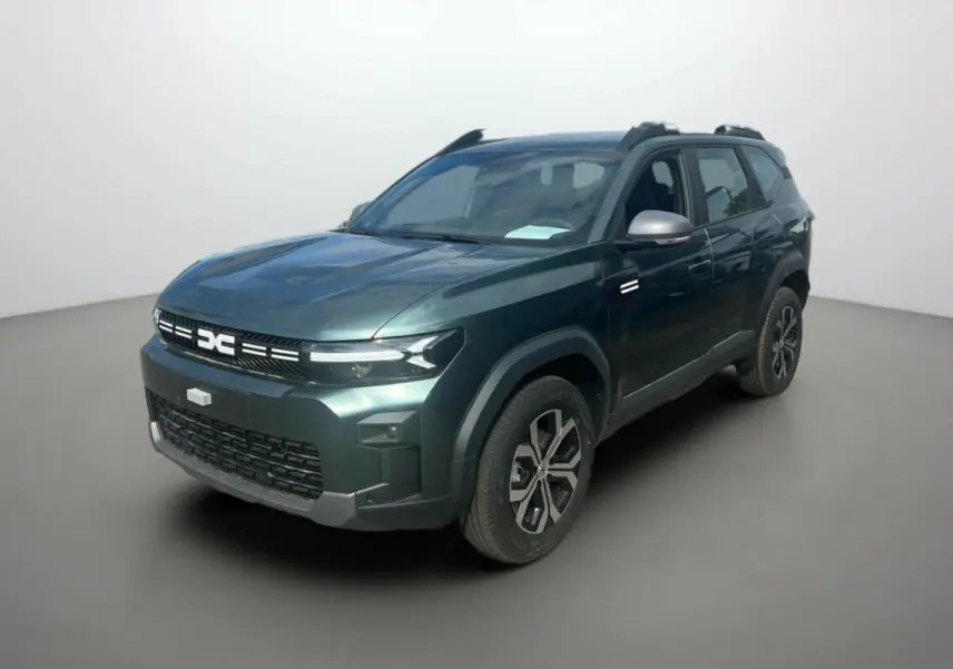 SUV Dacia Bigster vert cèdre en 3/4 avant droit, avec barres de toit et jantes alu 17 pouces visibles.