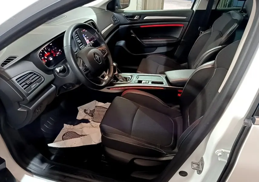 Vue intérieure côté conducteur de la Renault Mégane Techno TCe 140 blanche, avec tableau de bord et sièges noirs.