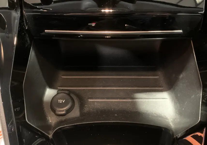 Gros plan sur la prise 12V et le rangement central noir de l’habitacle de la Peugeot 208 gris, version PureTech 100 Allure Business.