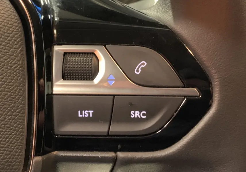 Gros plan sur les commandes au volant côté gauche de la Peugeot 208 gris, avec boutons LIST, SRC et téléphone.