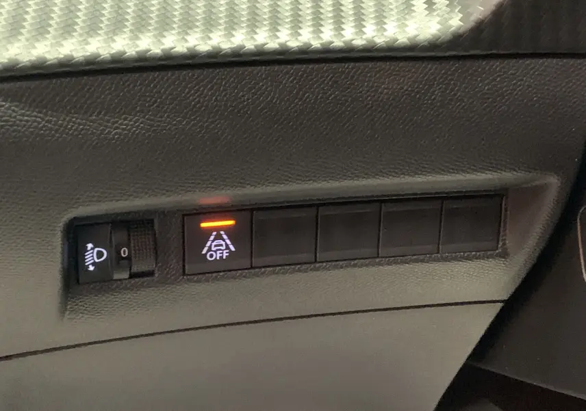 Gros plan sur les commandes de réglage des phares et de désactivation de l'alerte de franchissement de ligne dans une Peugeot 208 gris 2021.