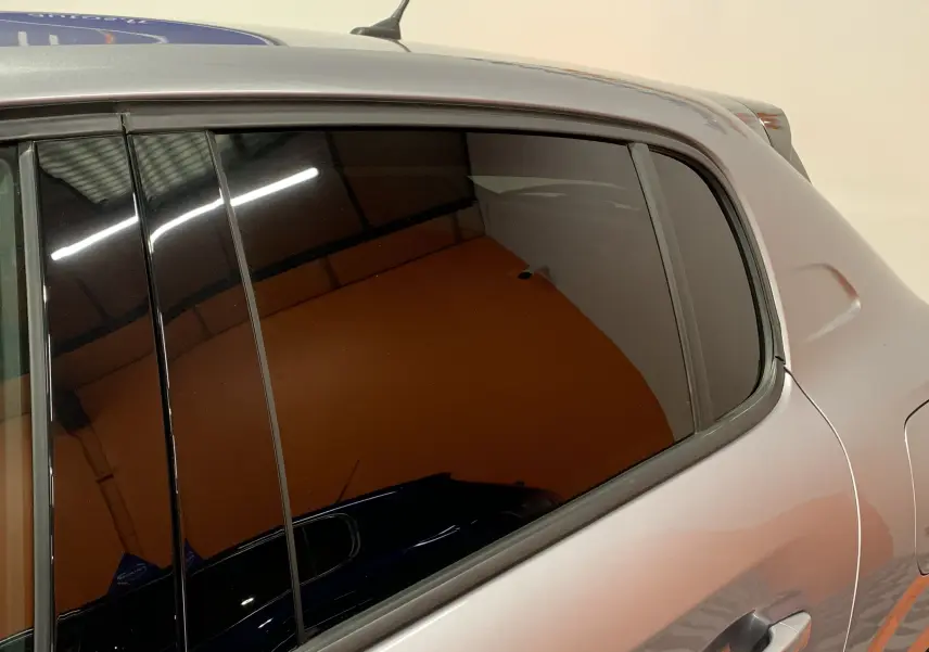 Vue rapprochée du côté gauche arrière d'une Peugeot 208 PureTech 100 Allure Business gris avec vitre teintée.