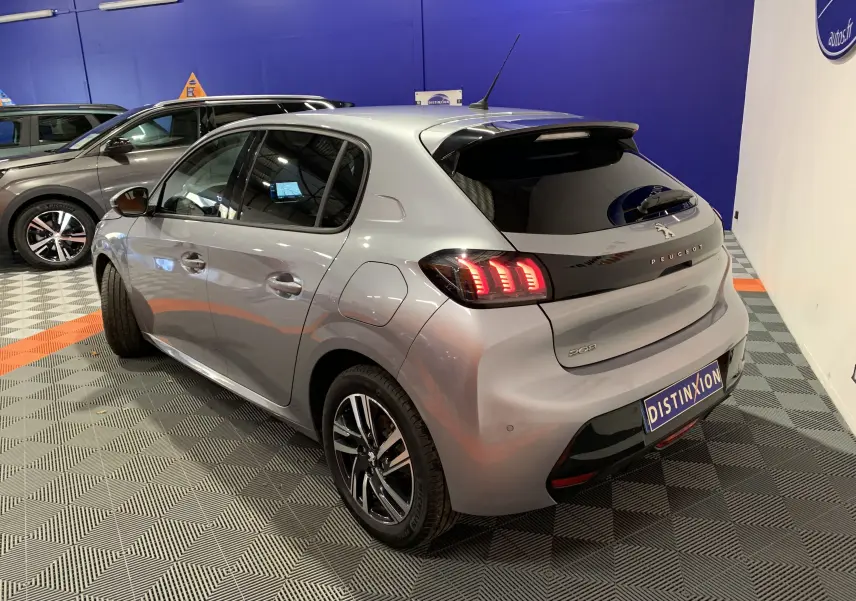 Vue 3/4 arrière droite d'une Peugeot 208 gris métallisé avec feux arrière LED et toit noir en intérieur showroom.