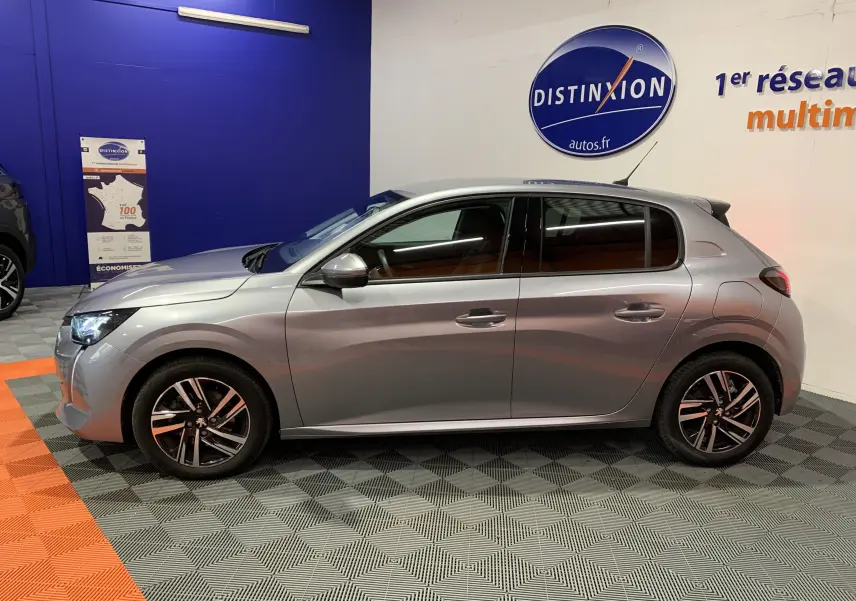 Profil droit d'une Peugeot 208 gris métallisé de 2021, finition Allure Business avec jantes alliage et phares LED allumés.