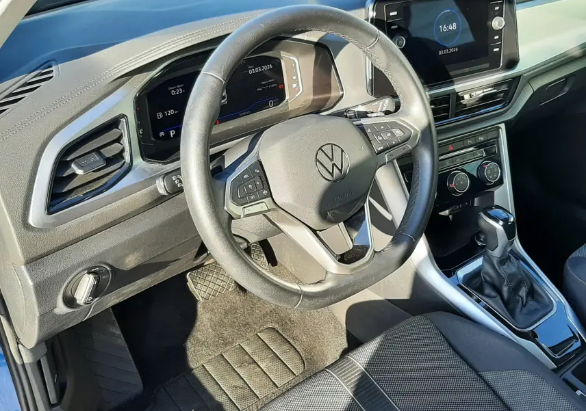 Vue intérieure côté conducteur du Volkswagen T-Roc bleu 2022, montrant volant multifonction, tableau de bord digital et console centrale avec boîte auto.