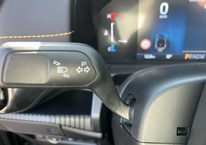 Gros plan sur la manette de clignotants et feux du Ford Ranger PHEV 281 Wildtrak, intérieur noir avec coutures marron.